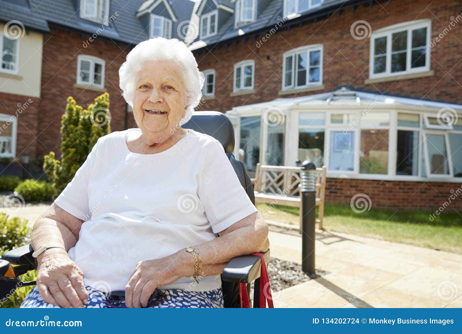 portrait of senior woman sitting outside retirement home in motorized wheelchair
