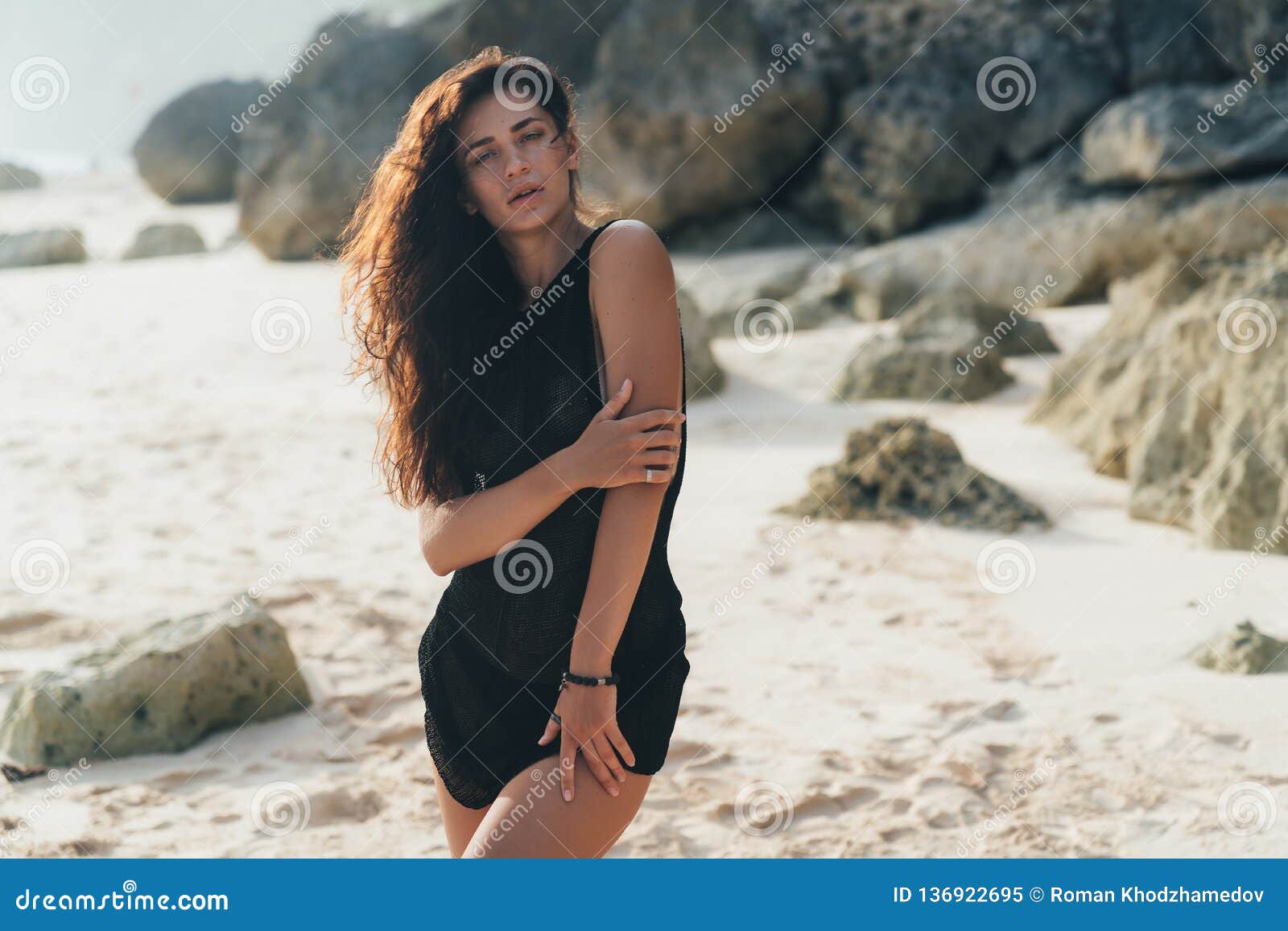 Portrait Of Brunette Model In Knitted Sweater Posing On The Sandy Beach Big Stones And Rock On 