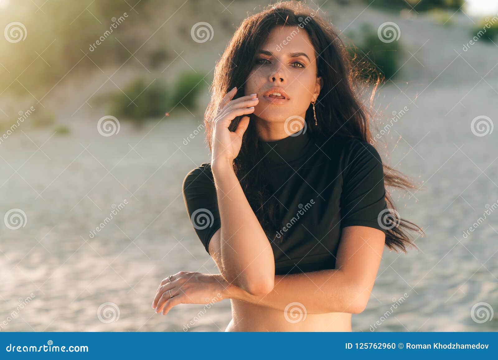 Portrait Of Sensual Girl Has Smooth Tanned Skin Posing On Beach Wind Blowing Her Thick Curly 