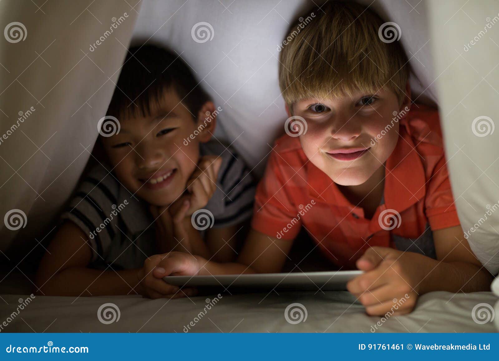 Portrait of Siblings Under Bed Sheet Using Digital Tablet on Bed Stock
