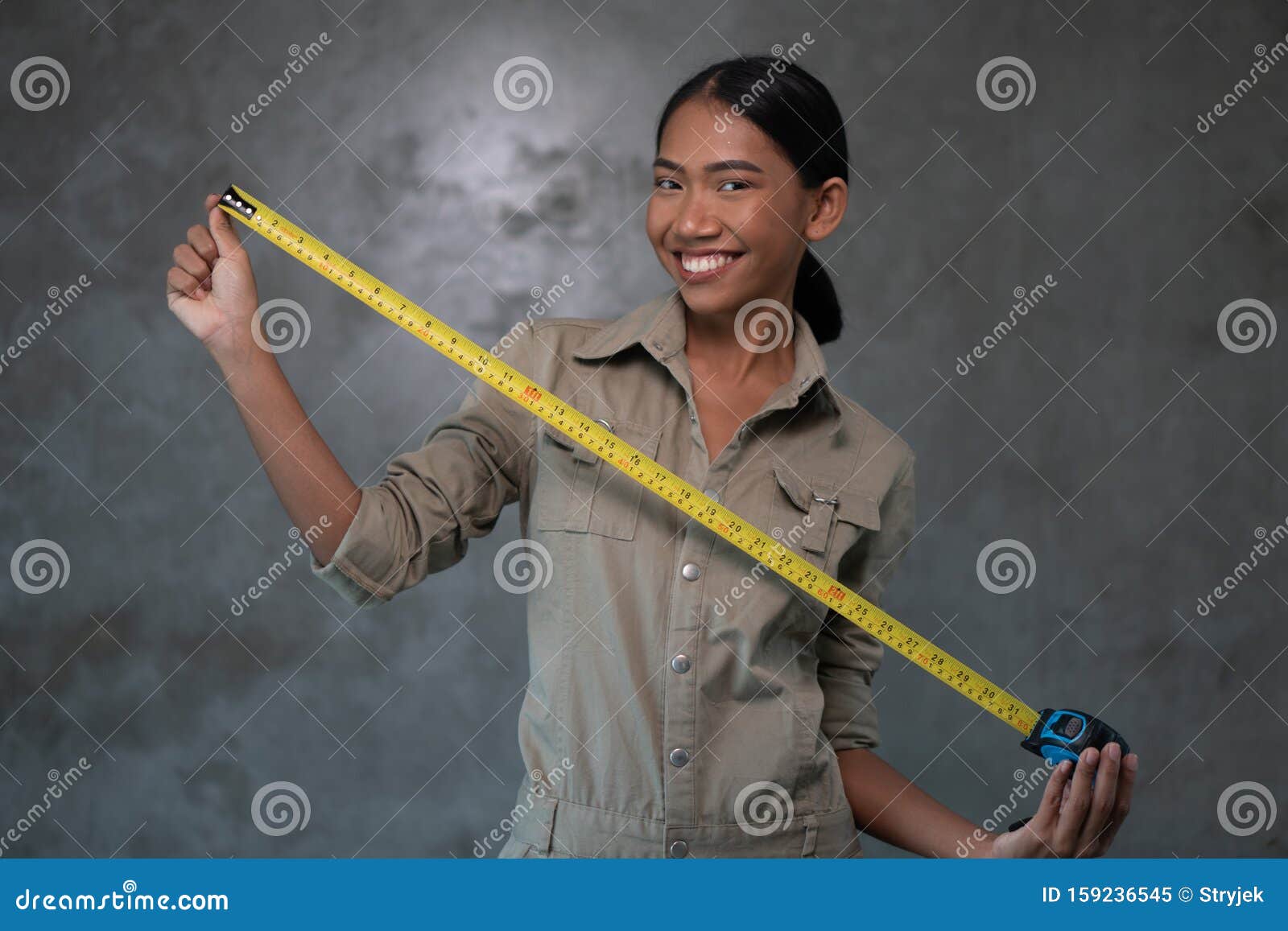 portrait of smiling asian woman architect holding measuring tape over concrete wall