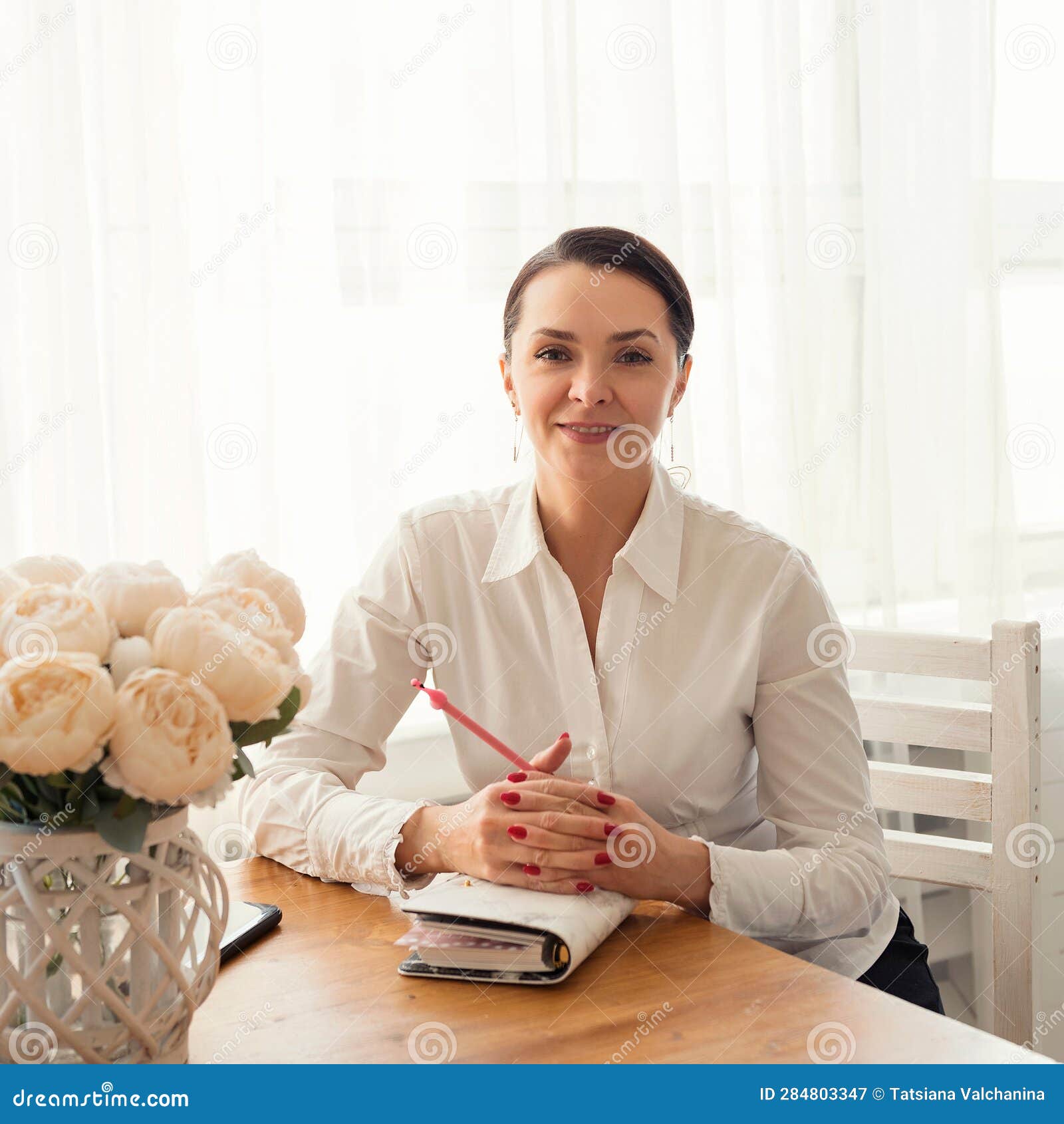 portrait of a smiling businesswoman sitting at a table with a notebook and a pen