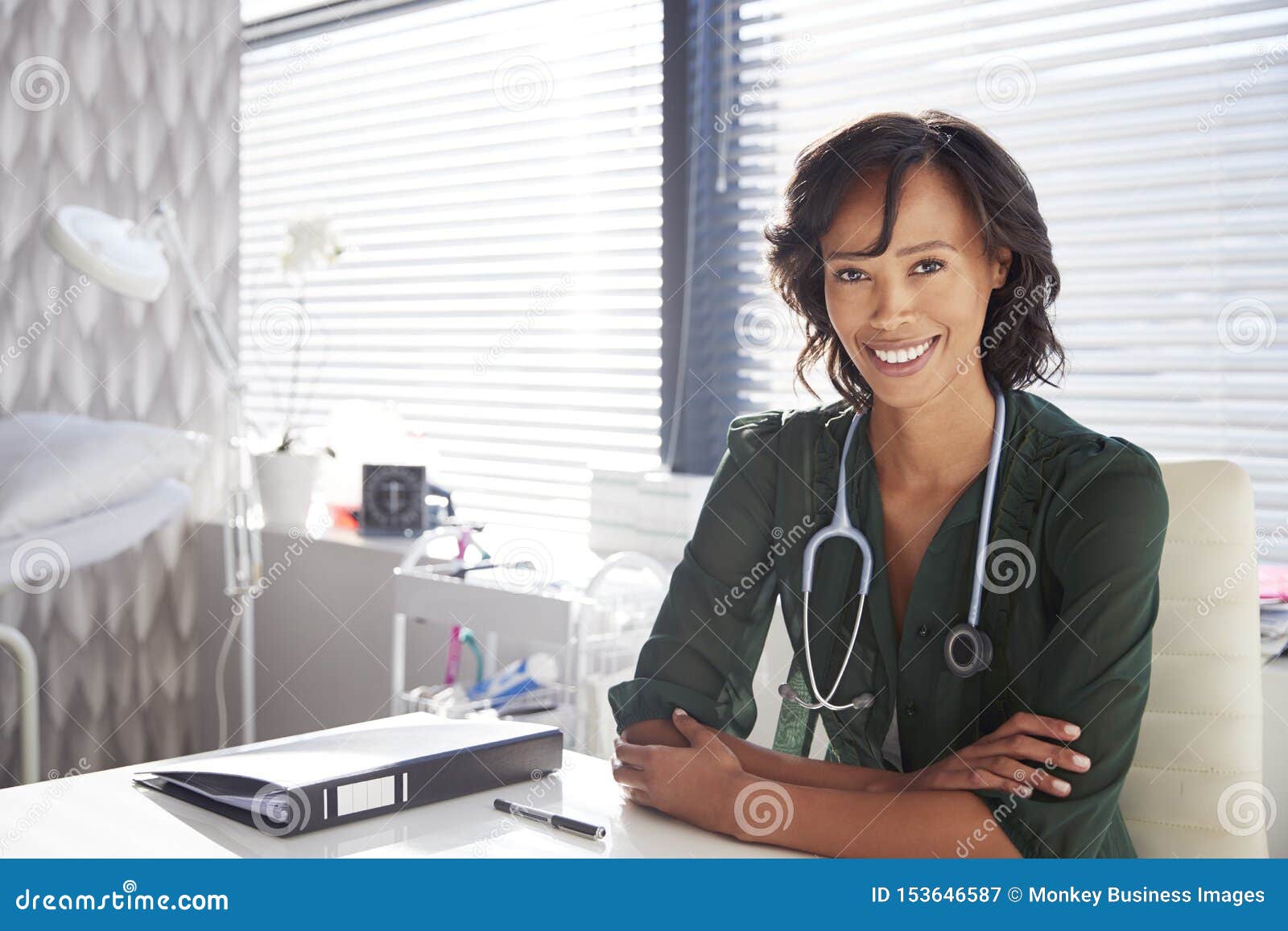 portrait of smiling female doctor with stethoscope sitting behind desk in office