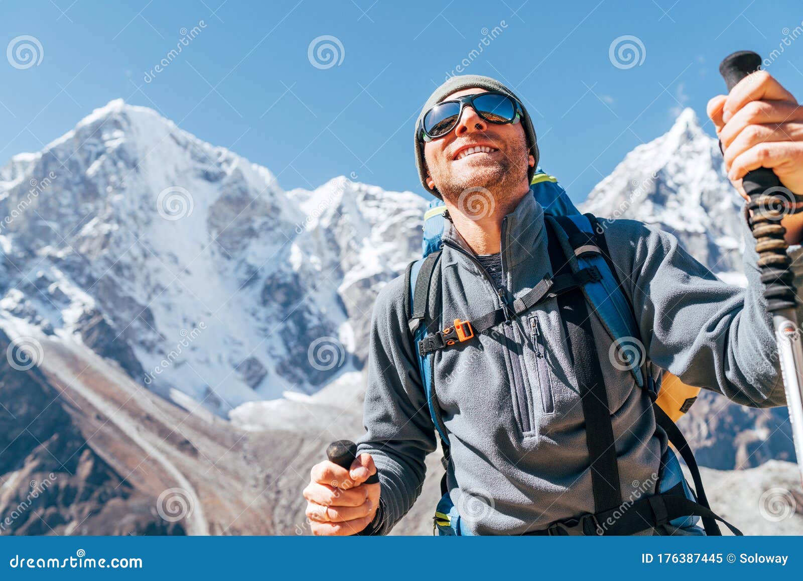 portrait of smiling hiker man on taboche 6495m and cholatse 6440m peaks background with trekking poles, uv protecting sunglasses.