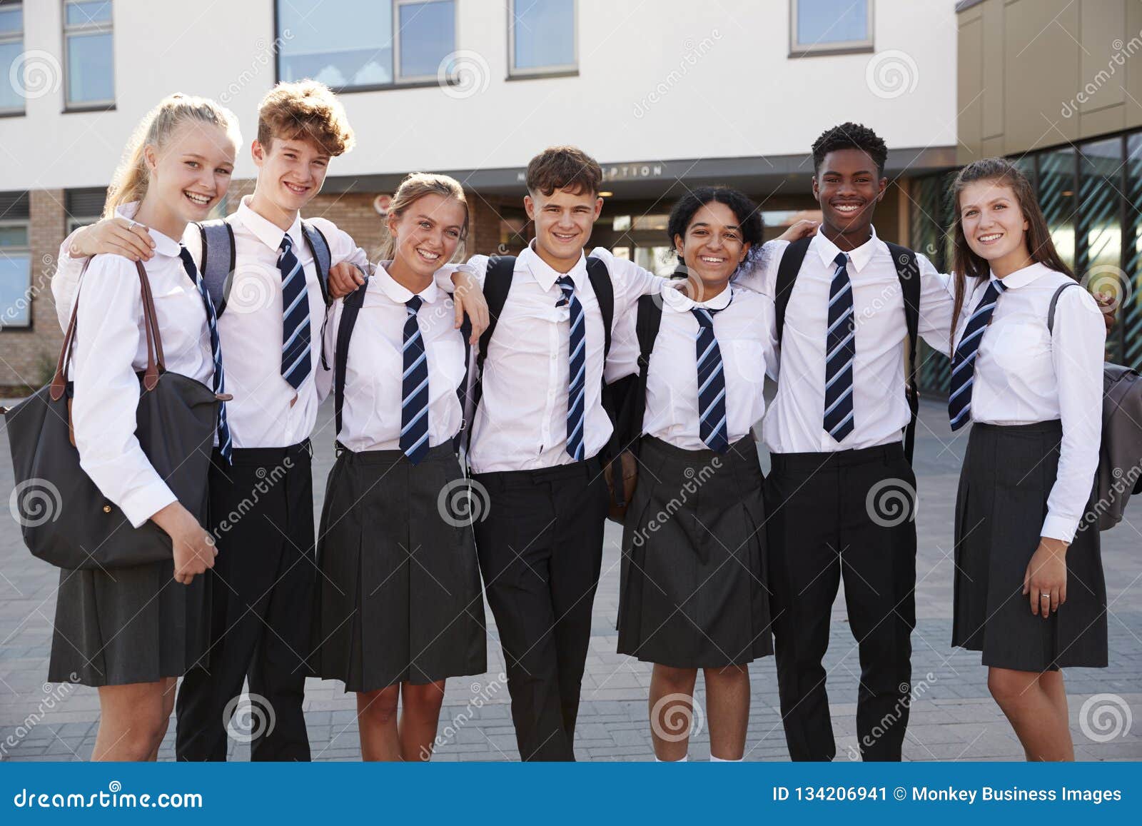 portrait of smiling male and female high school students wearing uniform outside college building