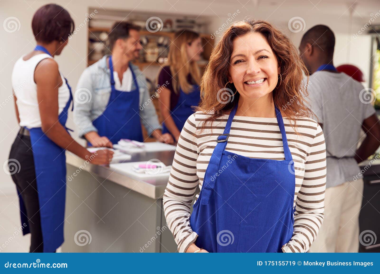 portrait of smiling mature woman wearing apron taking part in cookery class in kitchen