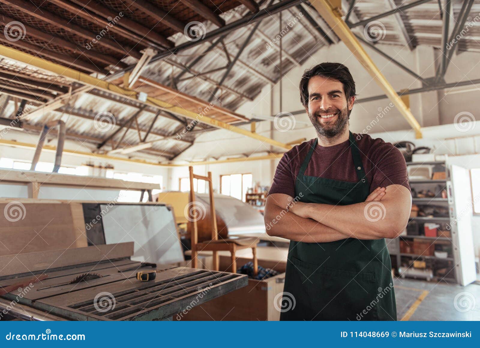 smiling woodworker standing in his workshop by a bench saw