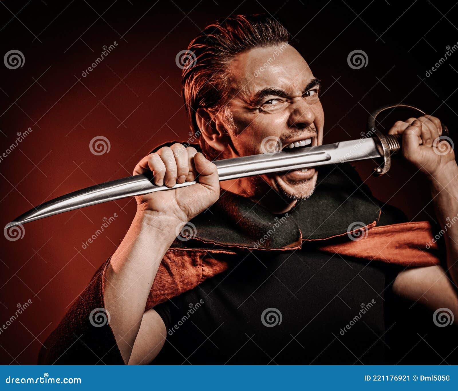 portrait of strong courage fervor man warrior in cape holding sabre, sword in his mouth, ready to fight over red