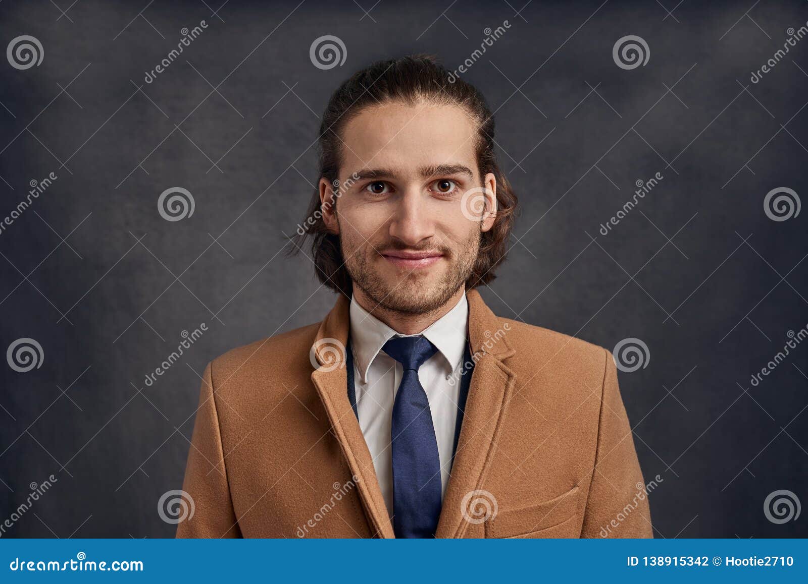 Portrait of a stylish young handsome man. Portrait of a stylish young handsome long-haired unshaven man in light brown blazer and blue necktie, looking at camera with friendly face