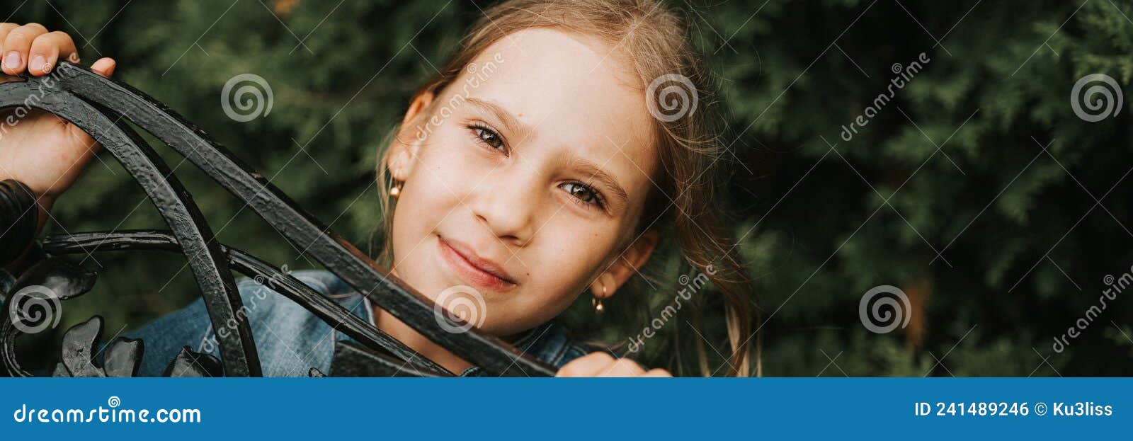 portrait thoughtful serious candid eight year old kid girl face peeking out of abstract metal s in nature. prepubertal age of