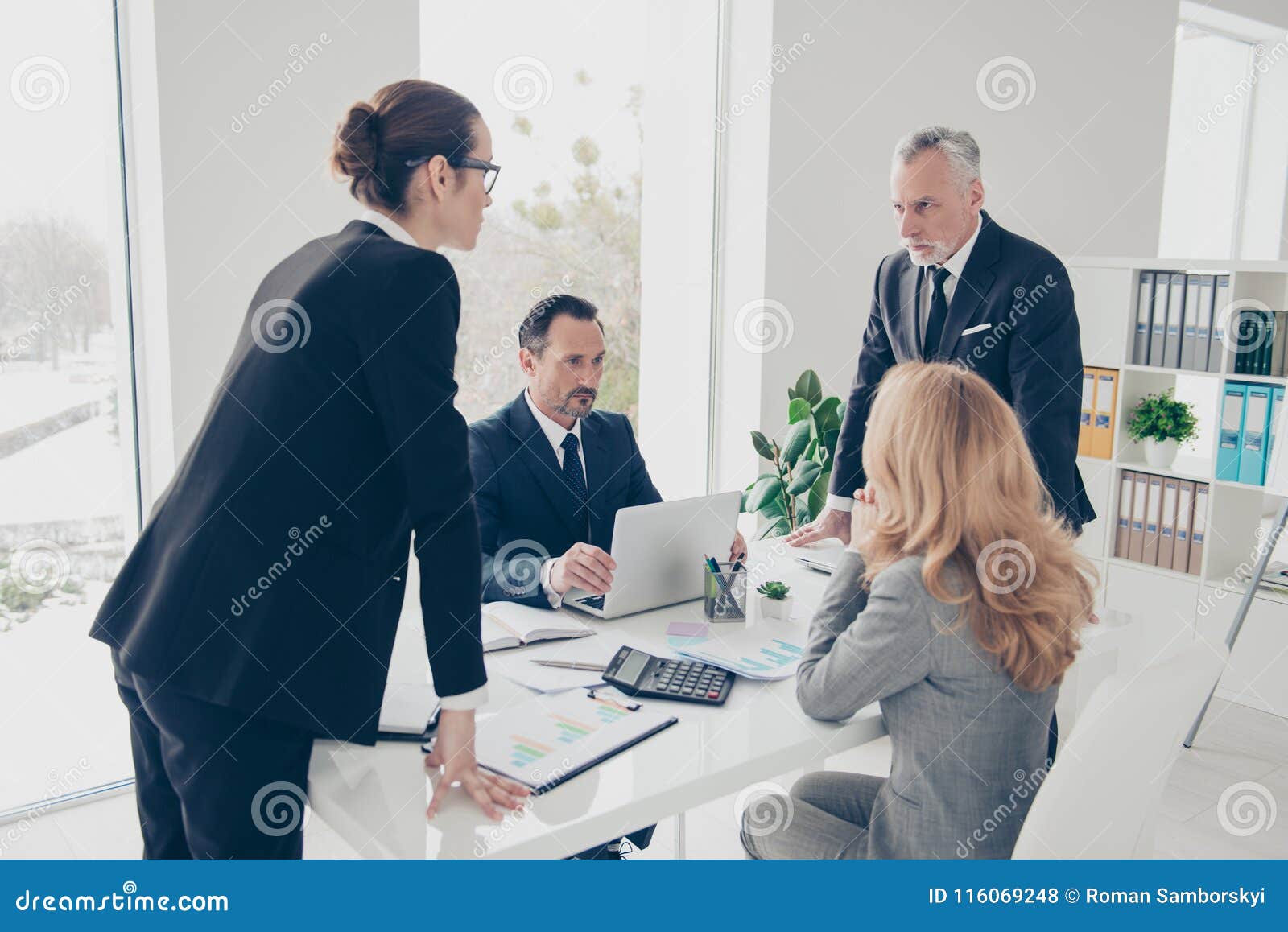 portrait of two stylish business persons in suits having disagreement, war, conflict, standing near desktop in front of each