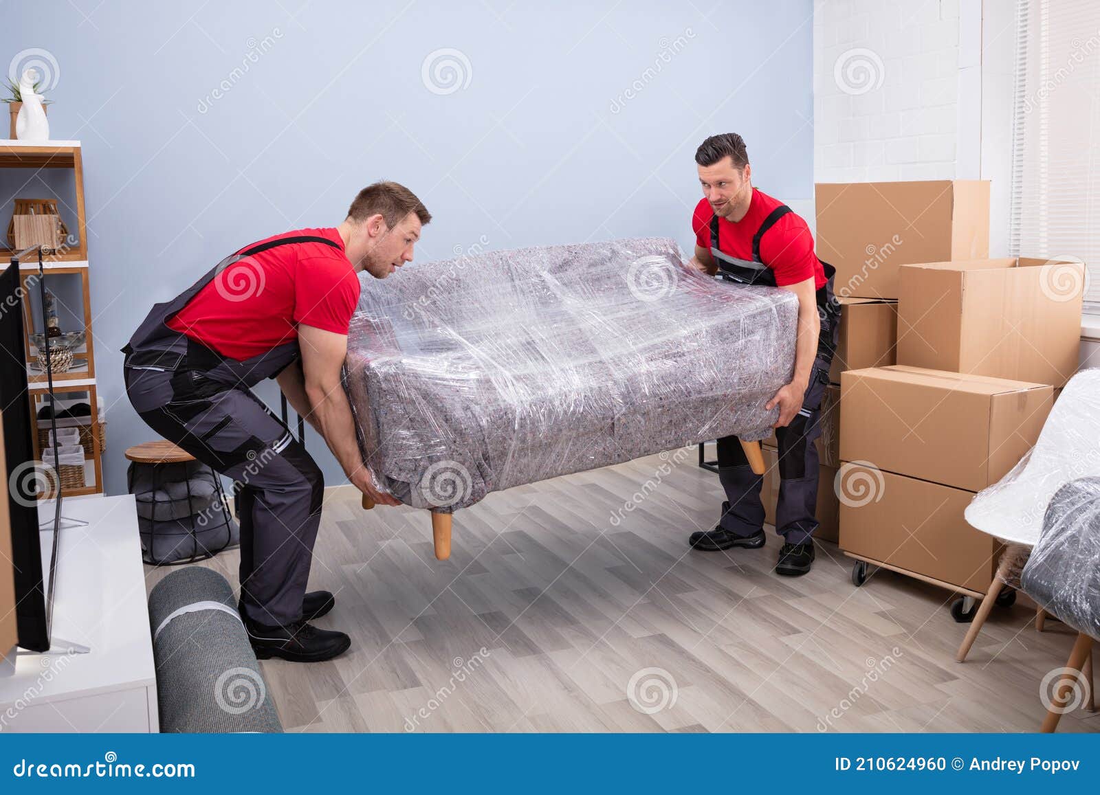 male movers carrying wrapped sofa in new house