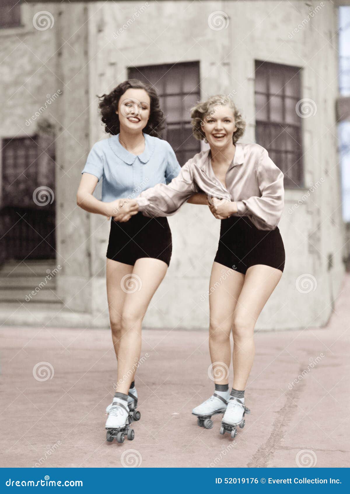 portrait of two young women with roller blades skating on the road and smiling