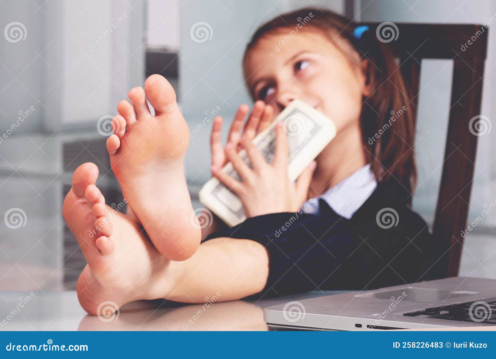 portrait of very happy cute young business girl with bare feet on the table and counts money profit. selective focus on feet