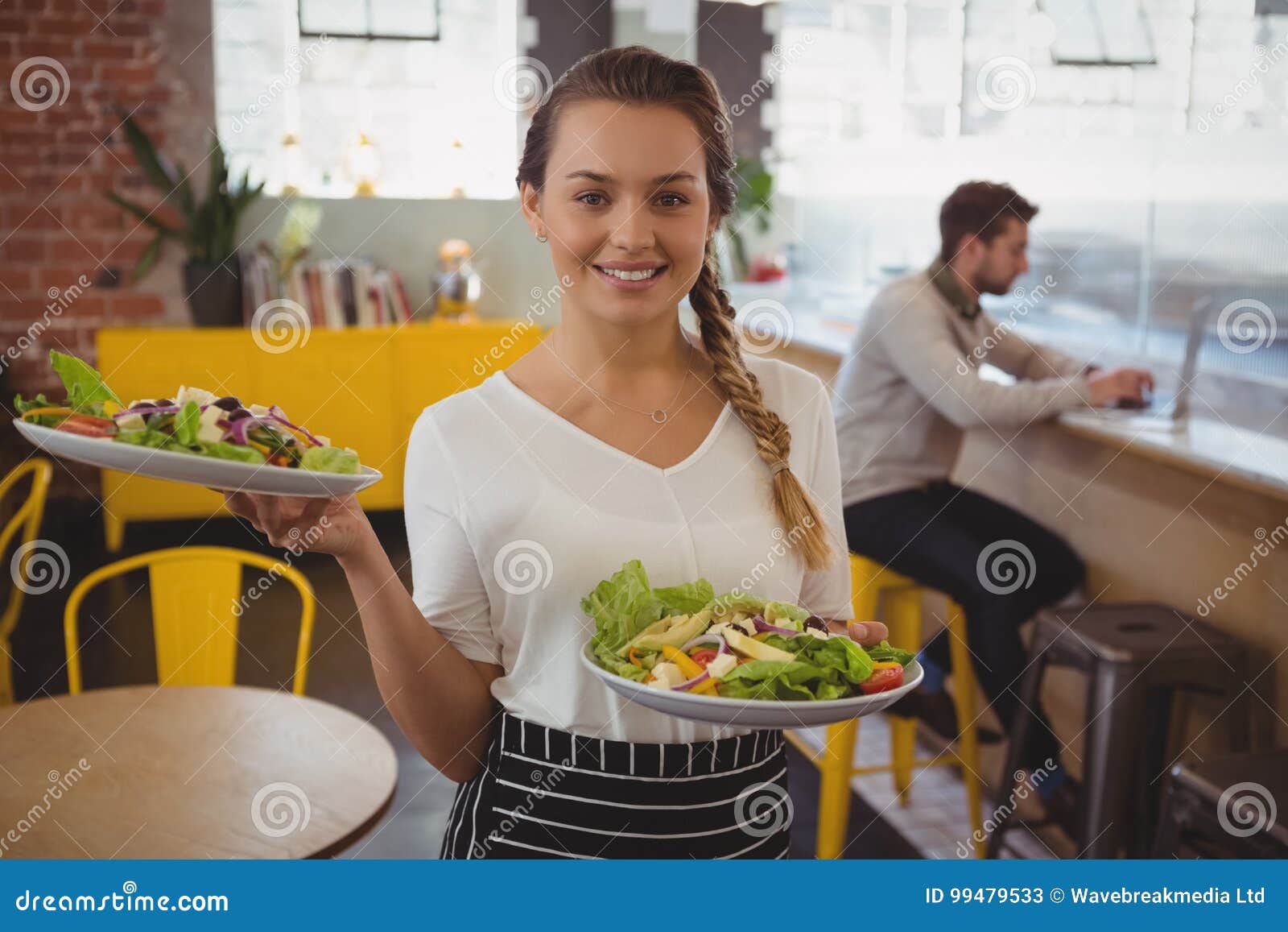 portrait of waitress holding plates with salad while businessman using laptop