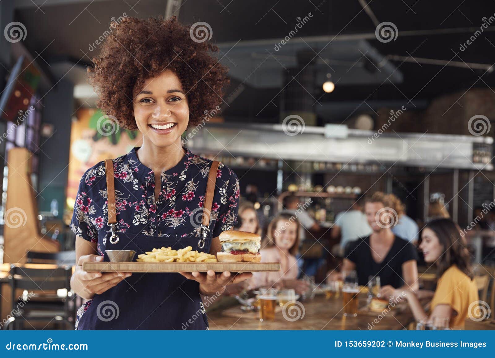 portrait of waitress serving food to customers in busy bar restaurant