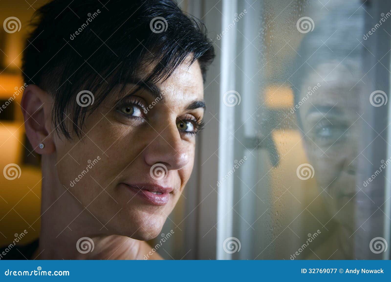 Portrait at the window. Side and shady head portrait a black-haired middle-aged woman looking thoughtful smiling into the camera