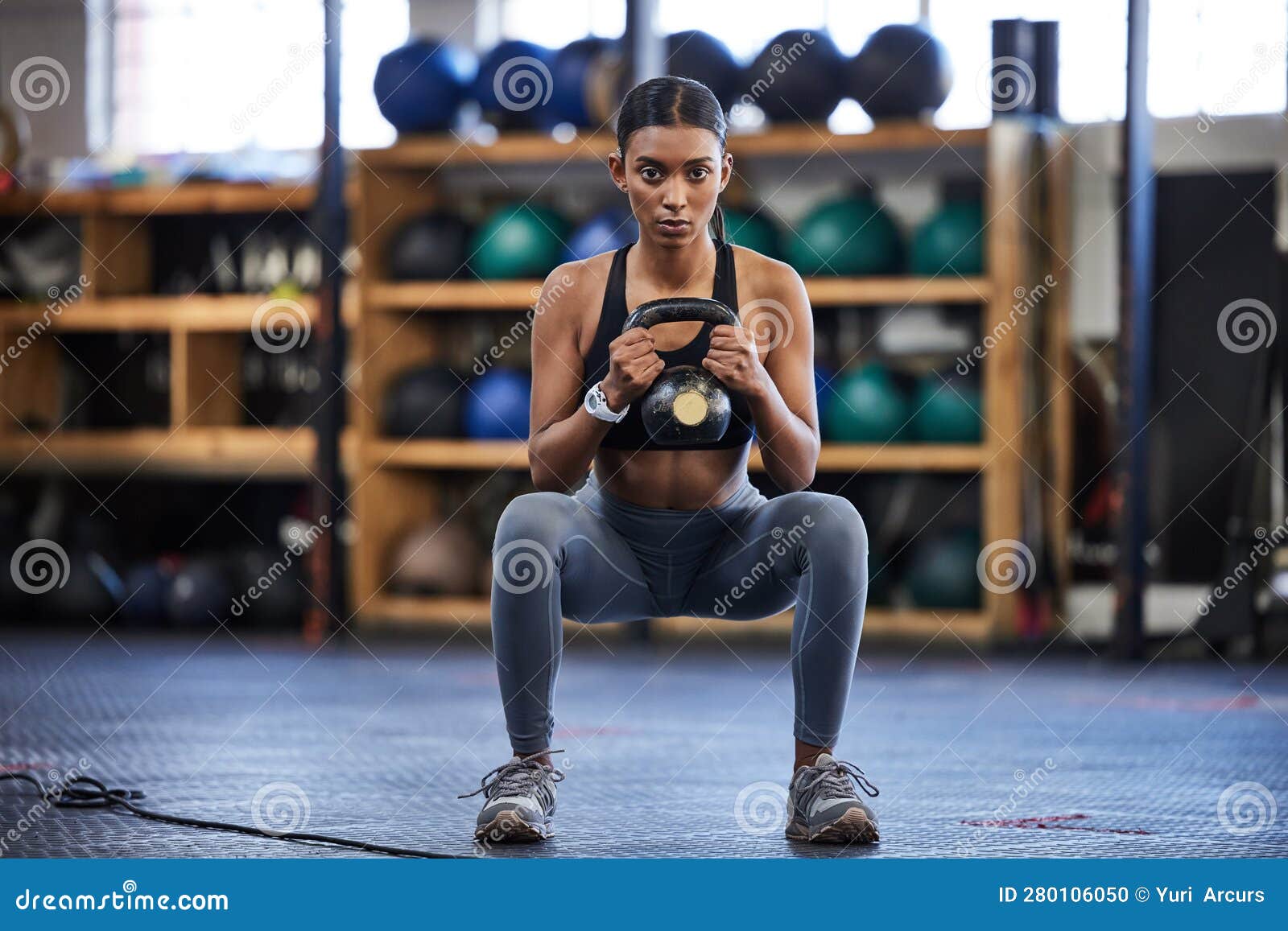 Woman practicing kettlebell squat with personal trainer at gym