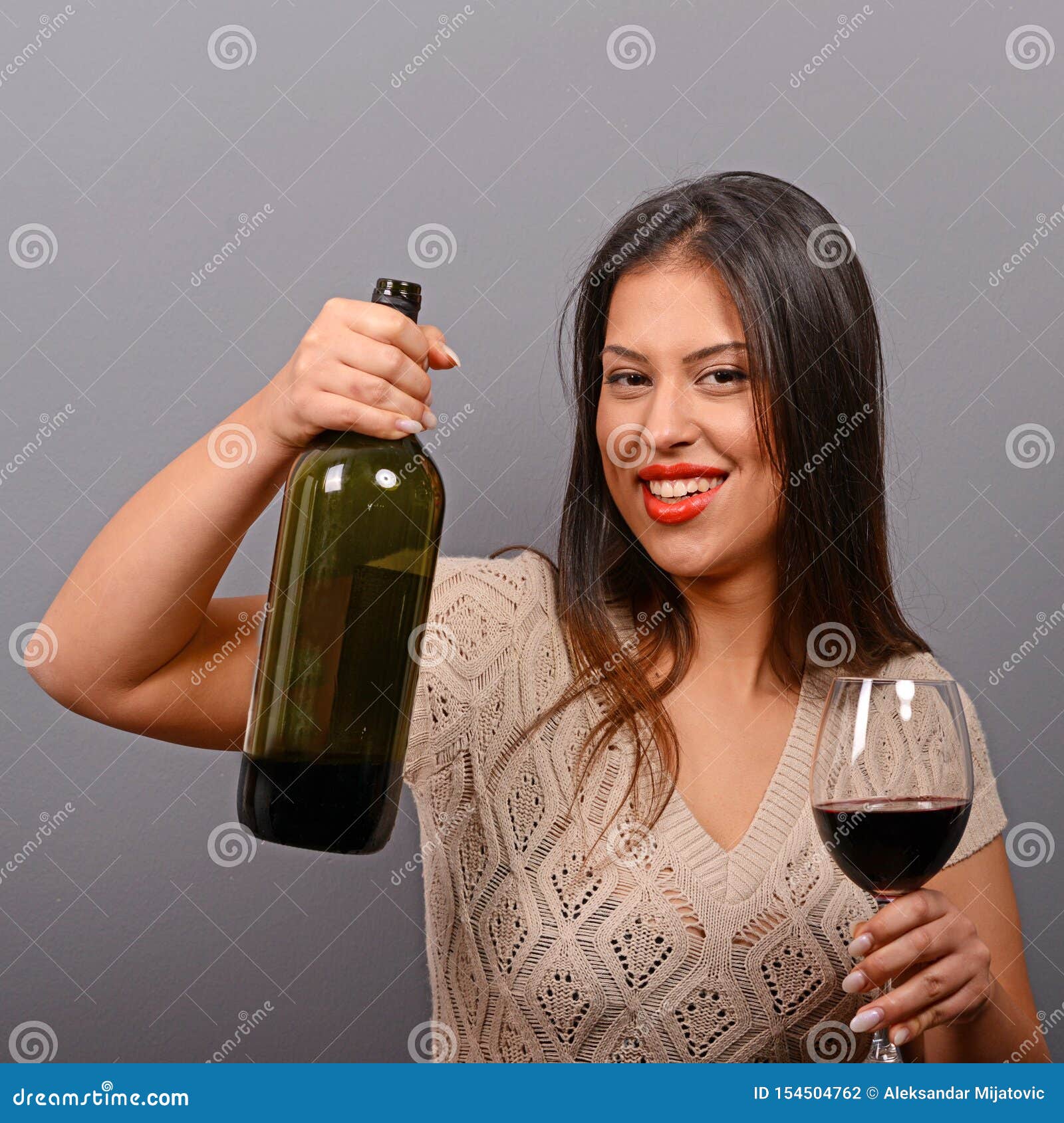 Portrait Of Woman Holding Wine Bottle And Glass Against Gray Background