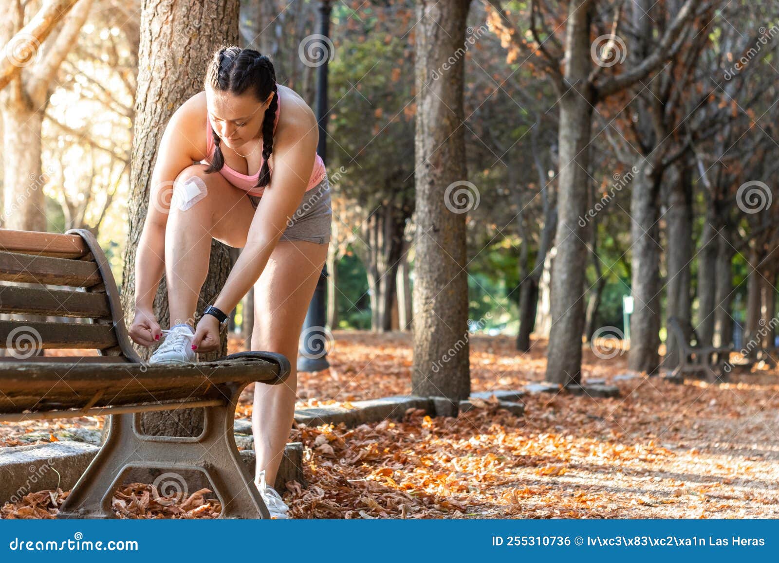 portrait of a woman lacing up her sneakers for sports in a park in autumn