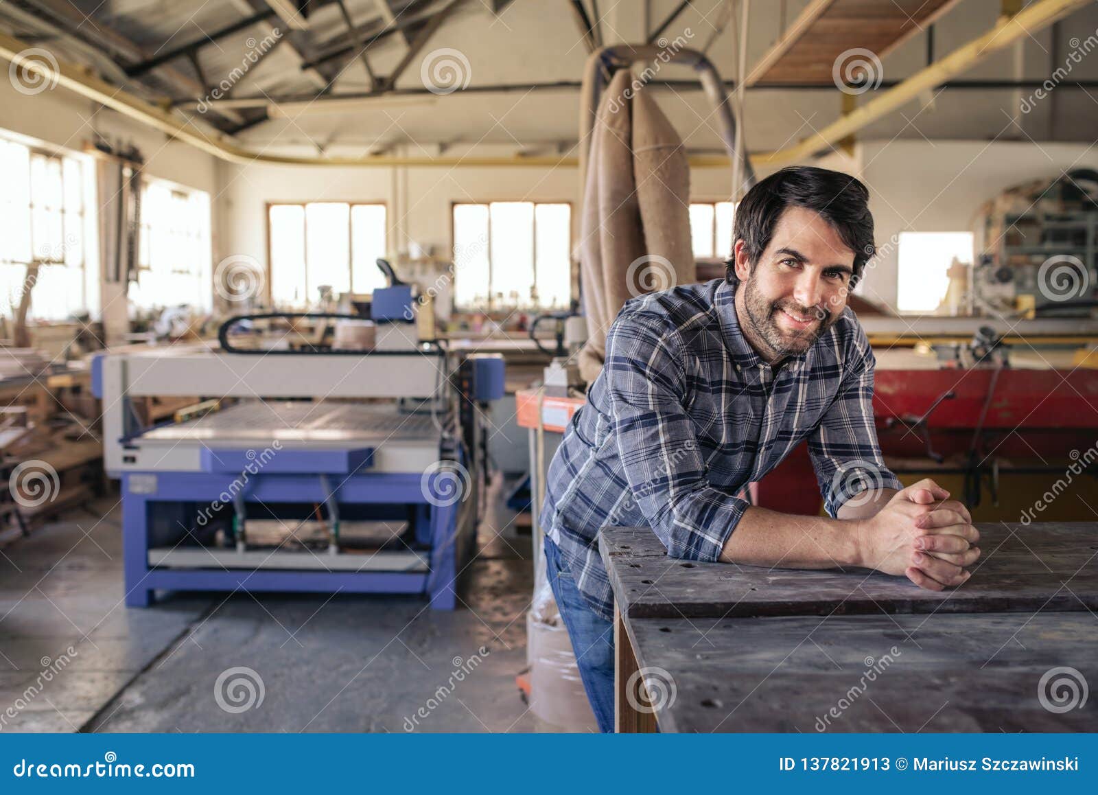 woodworker smiling while leaning on a bench in his workshop