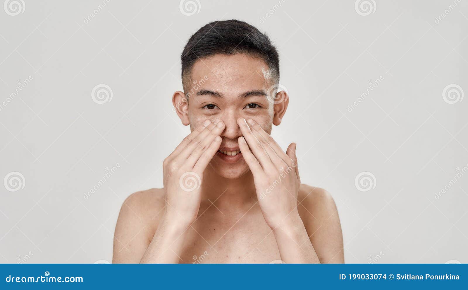 portrait of young asian man with problematic skin and hyperpigmentation looking at camera, applying cream on his face