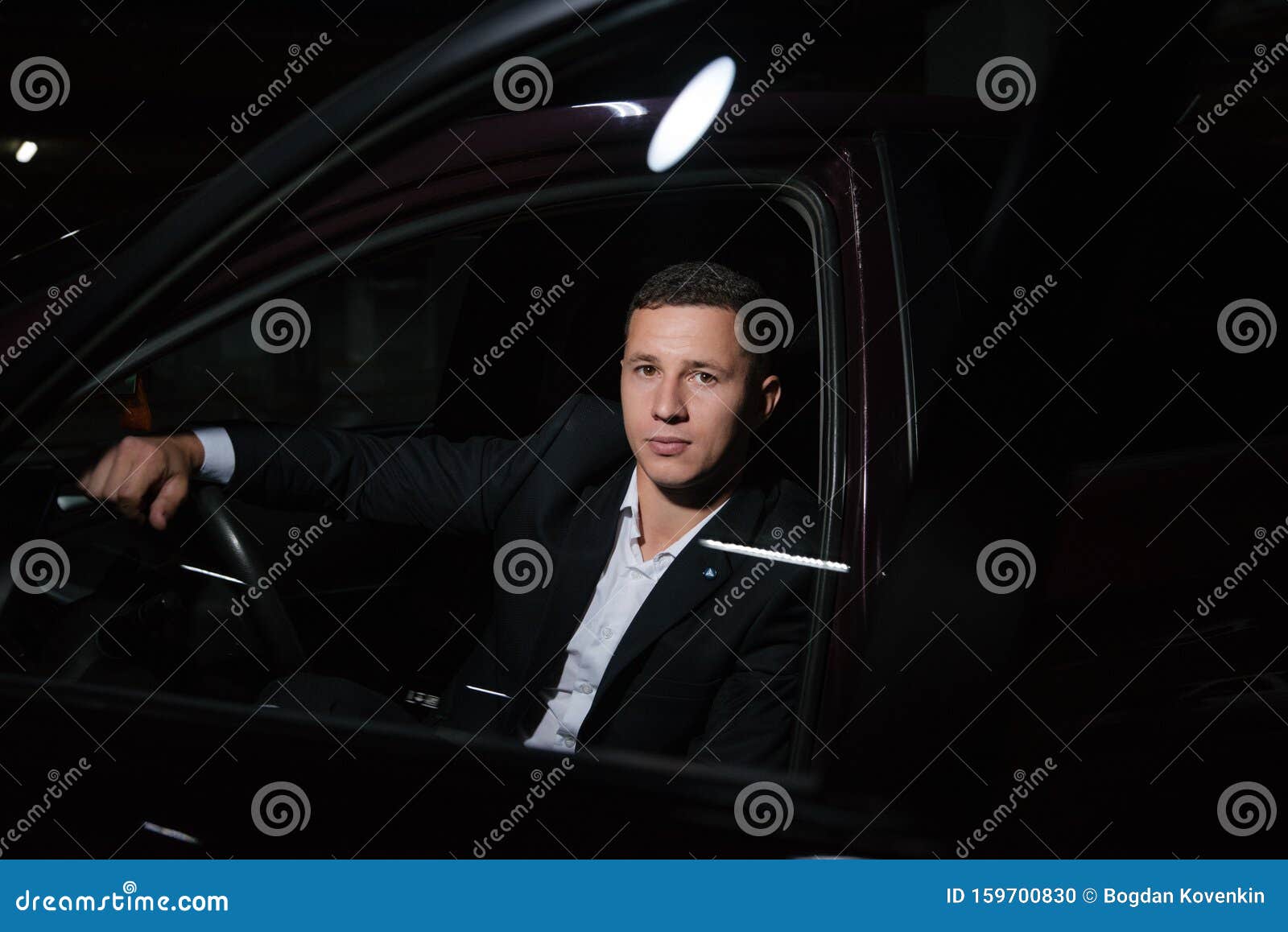 portrait of young attractiave man in suit sitting in his new stylish car