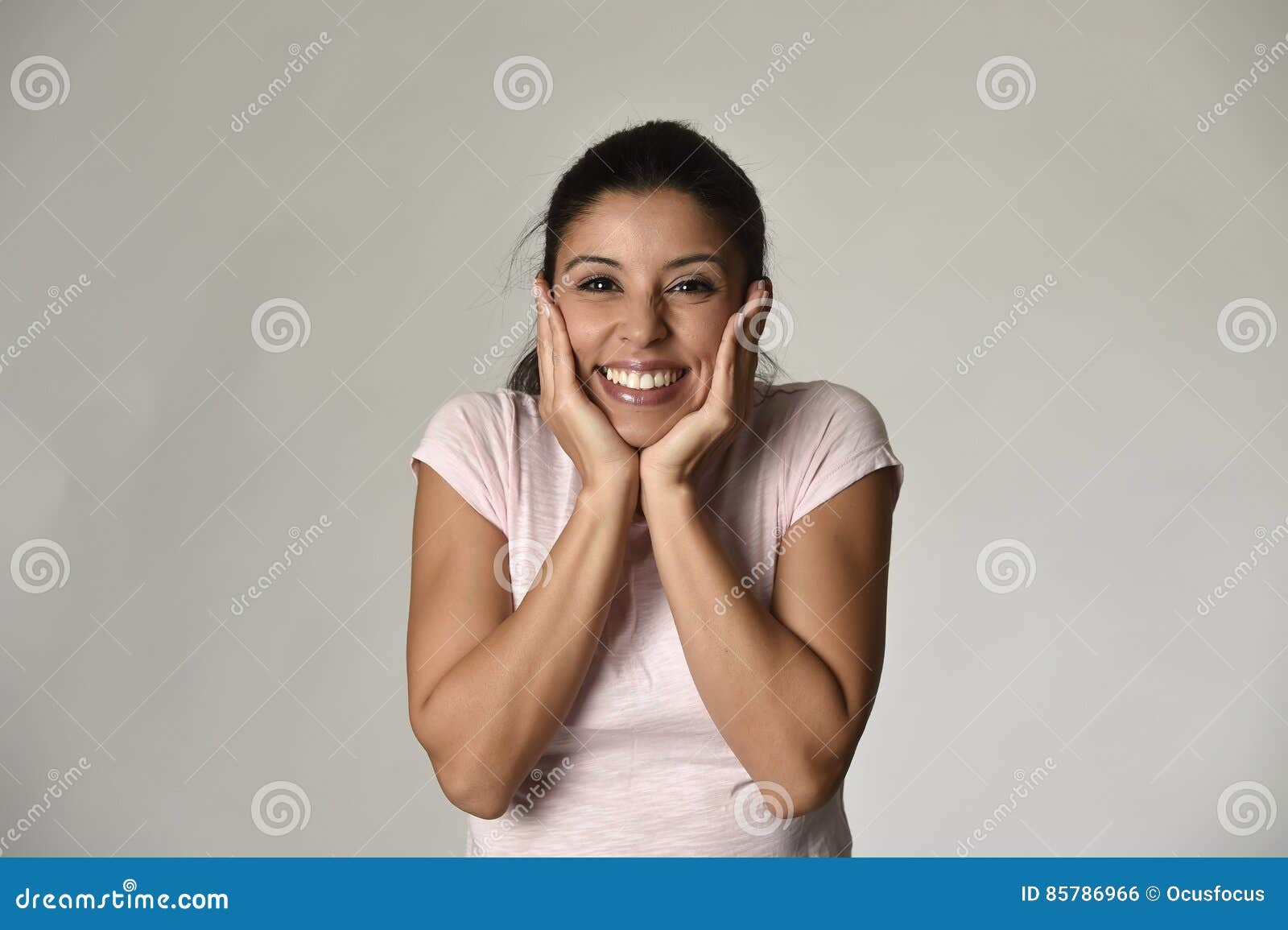 portrait of young beautiful and happy latin woman holding face with hands with big toothy smile