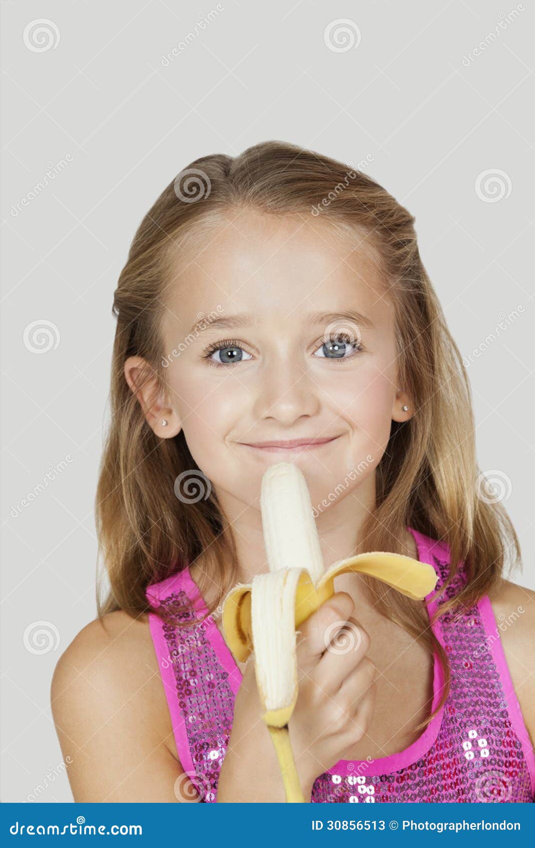 Portrait Of Young Girl Holding Banana Against Gray Backgro