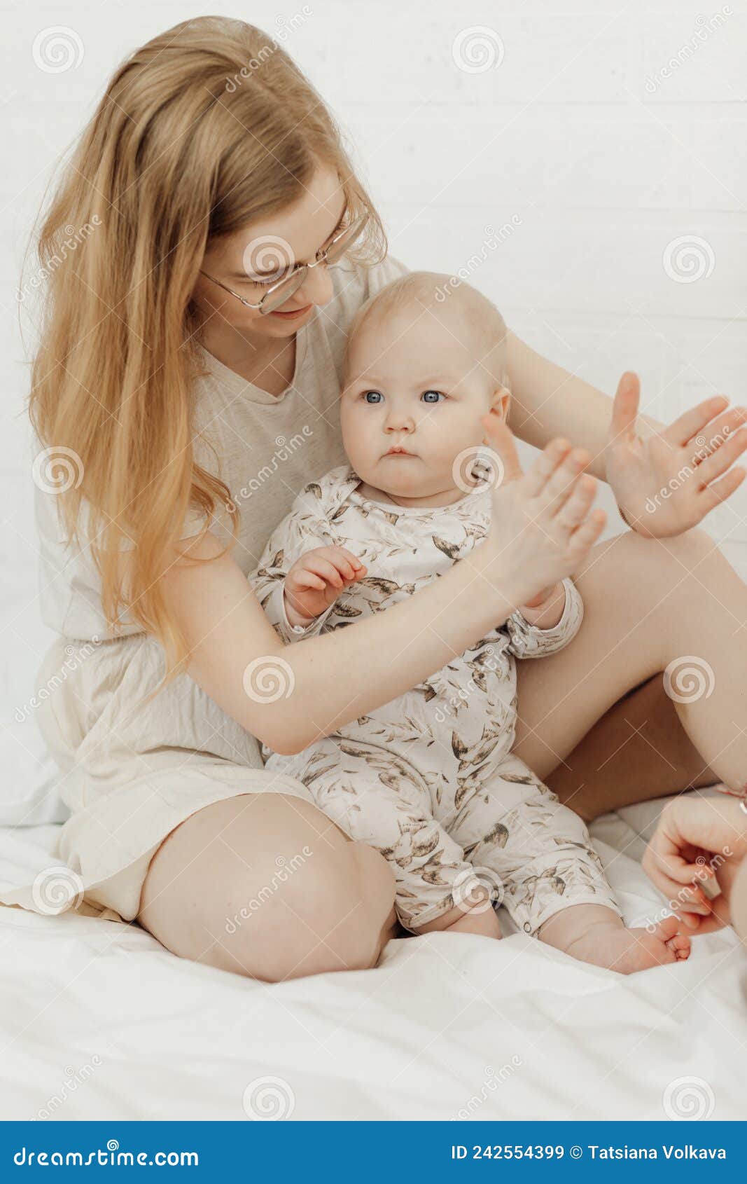 portrait of young happy smiling beautiful mother holding cute cherubic baby toddler in white clothe playing patty-cake.