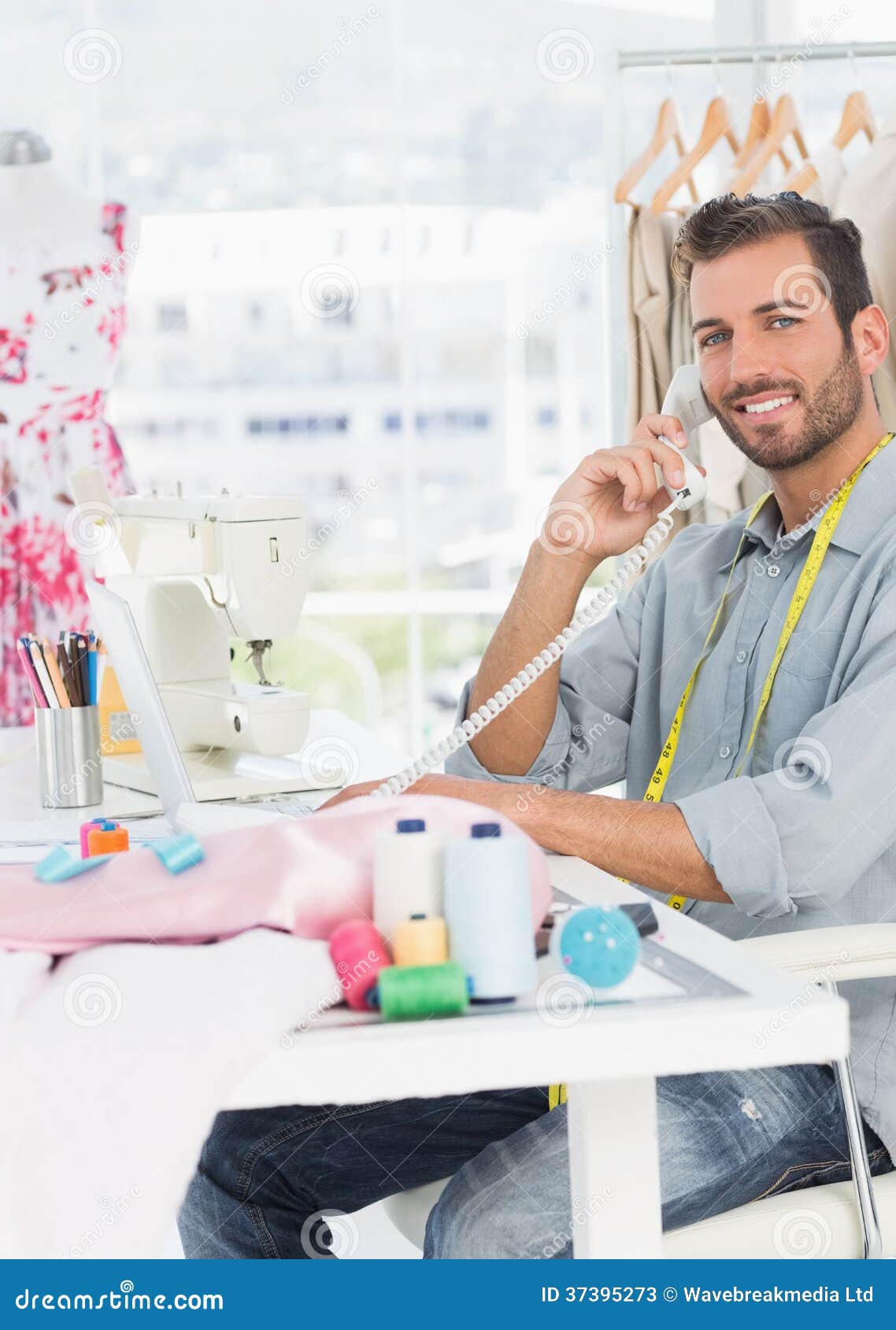 Side view portrait of a young male fashion designer using phone in the studio