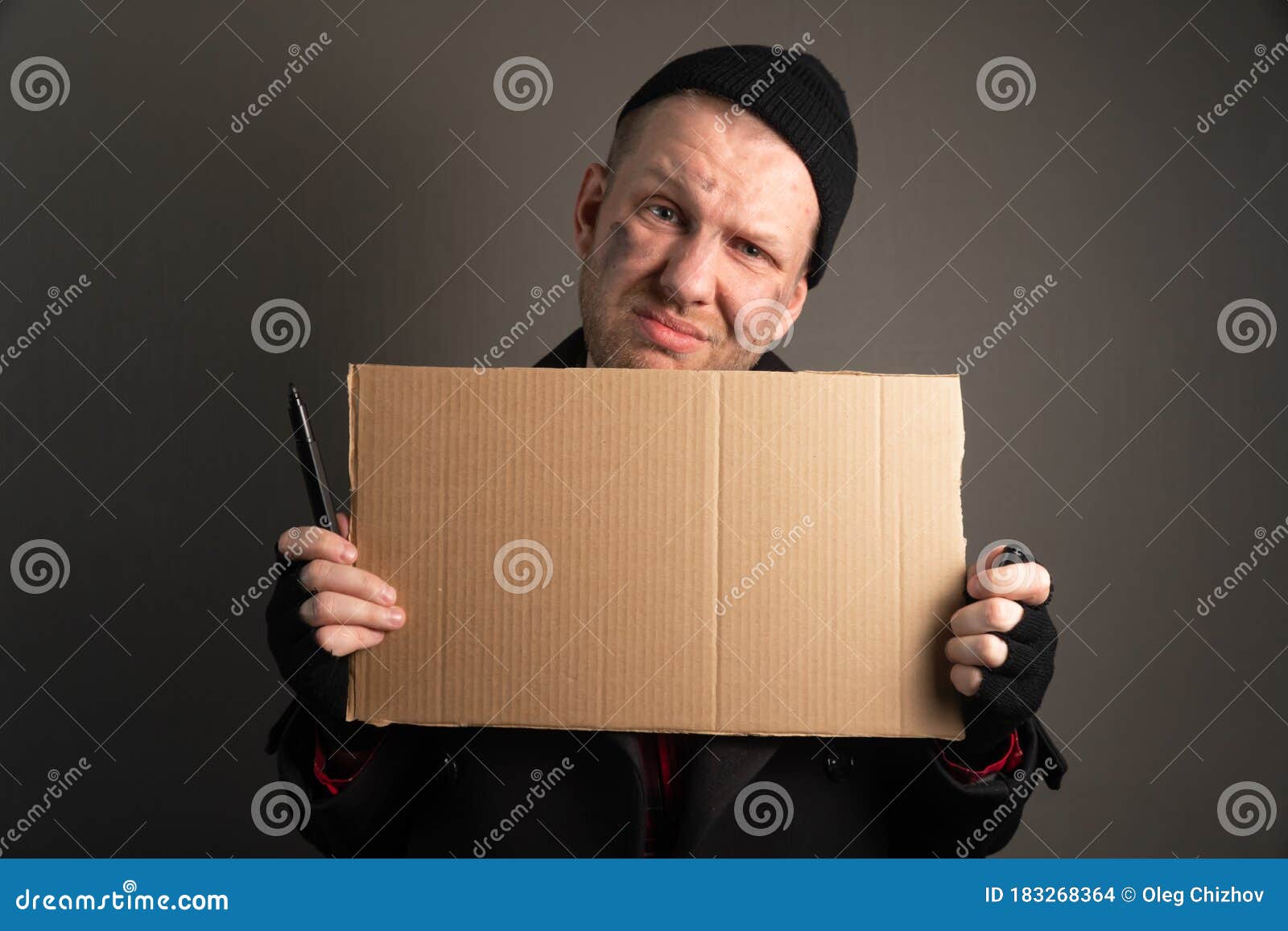 portrait a young man who holds a felttip pen in his mouth to write text on cardboard. begging concept