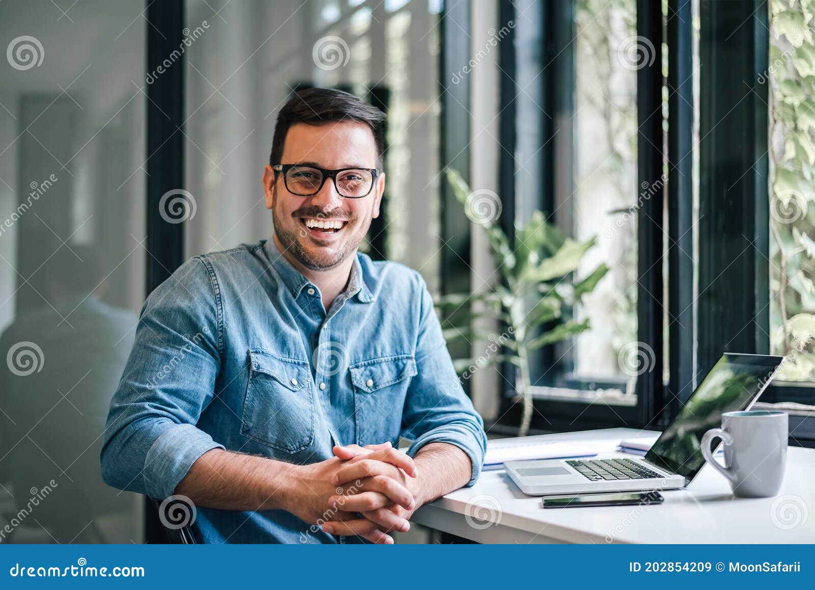 portrait of young smiling happy handsome successful businessman entrepreneur freelancer working from home office on laptop