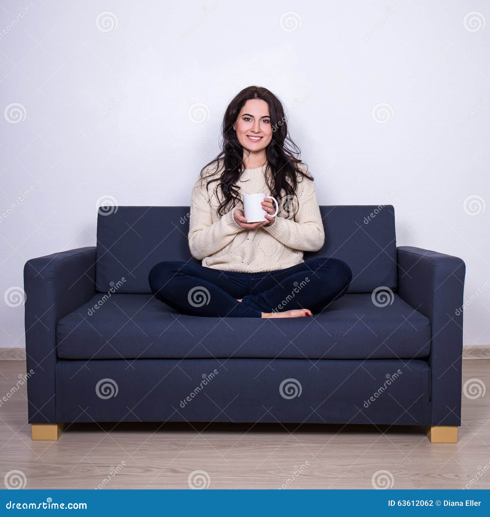 Portrait of young woman sitting on sofa with mug of tea or coffee at home