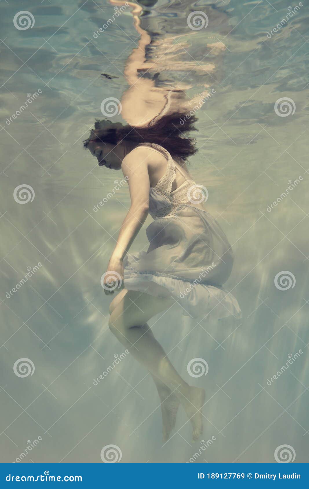 Portret van een meisje in een blauwe jurk die onder water drijft. Foto's van een jong meisje die onder water zwemt in een lichtblauwe jurk die het effect van gewichtloosheid en lichtheid creëert.