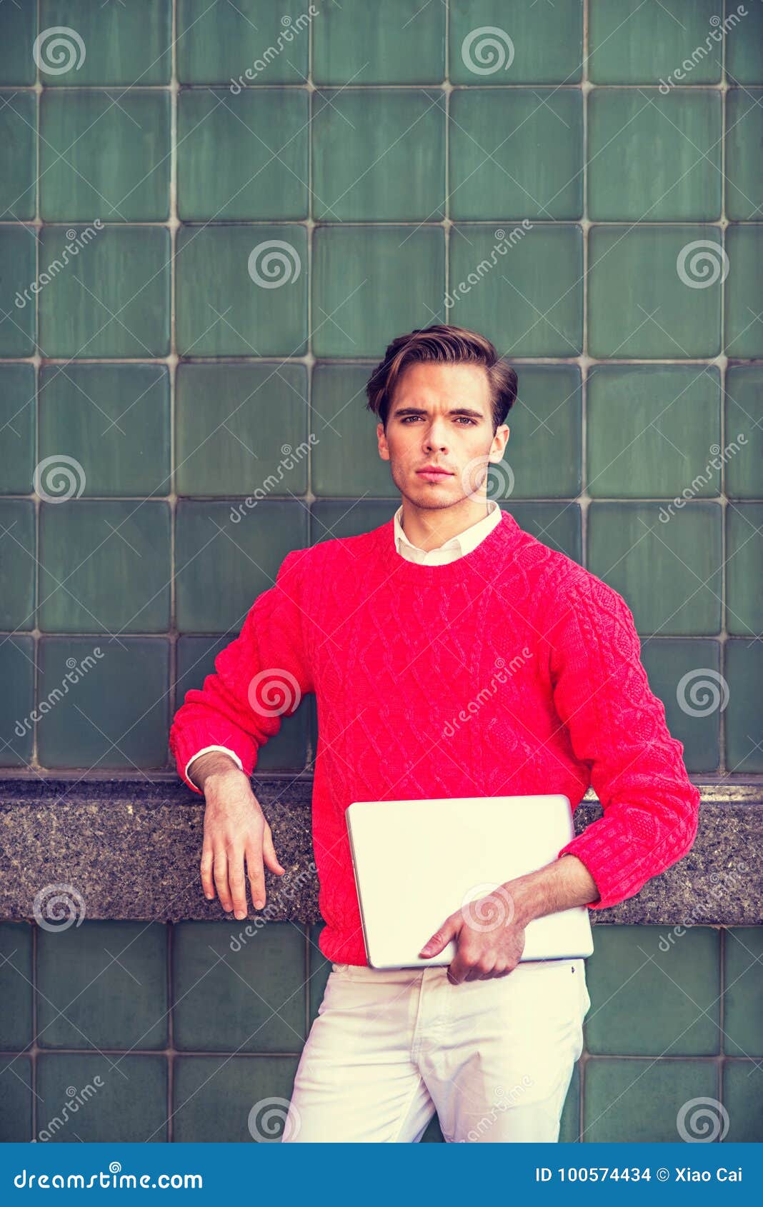Porträt des amerikanischen Studenten in New York. Der amerikanische Student, der in New York, tragender roter Strickpulli, weiße Hosen, Laptop-Computer halten, auf dem Campus stehend gegen grüne Wand, vorwärts schauend studiert, Instagram filterte Effekt