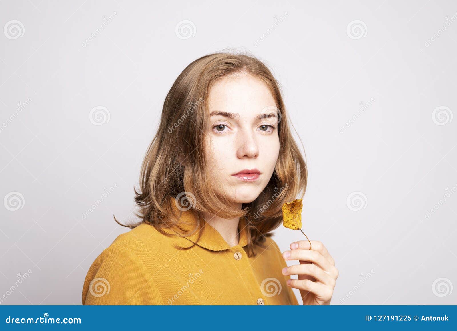 Porträt einer Schönheit in einem gelben Kleid. Herbstporträt einer schönen ungepflegten Frau in einem gelben Kleid mit einem getrockneten Blatt