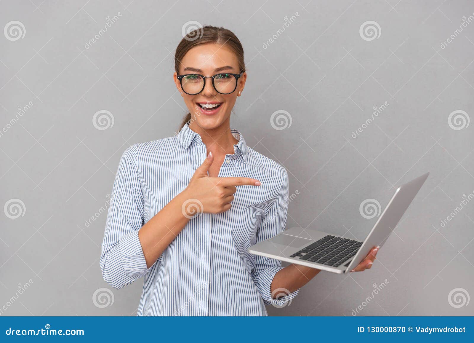 Pose heureuse gaie de jeune femme d'affaires d'isolement au-dessus du fond gris de mur utilisant le pointage d'ordinateur portabl