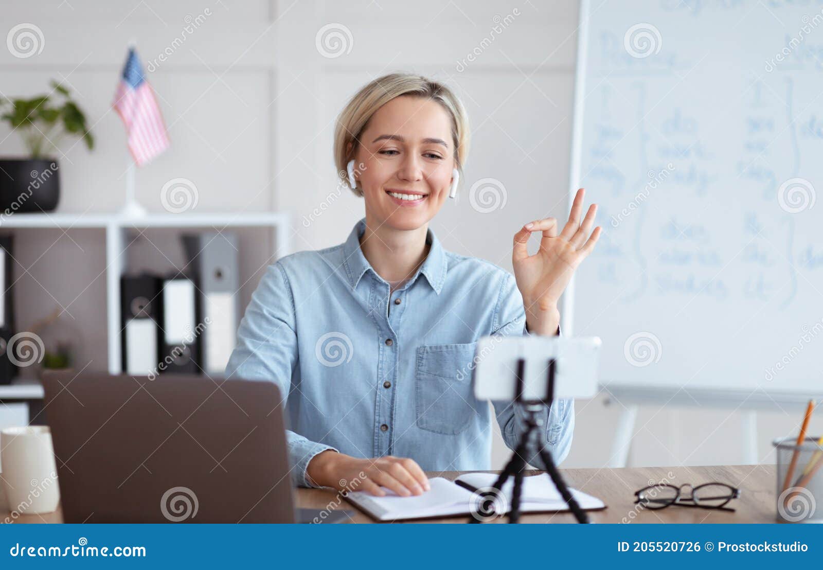 positive female teacher giving online english lesson on smartphone, showing ok gesture at home