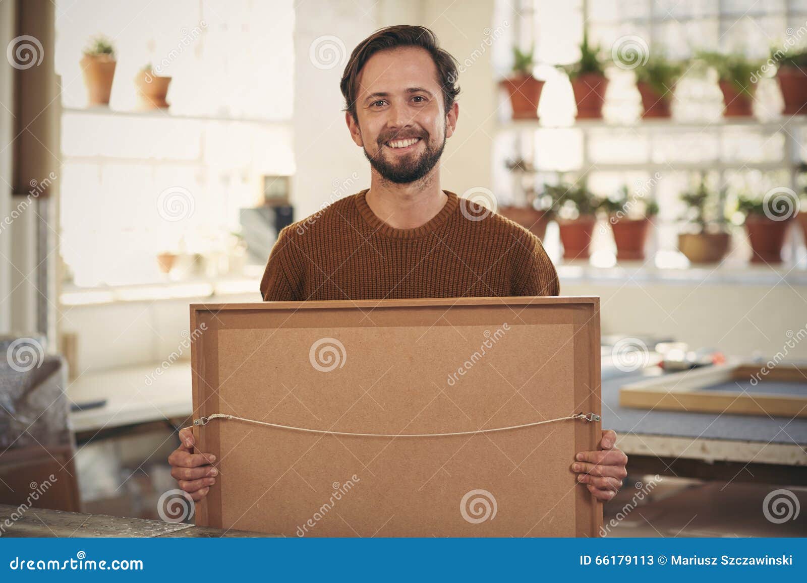 positive framer smiling his workshop holding a framed item