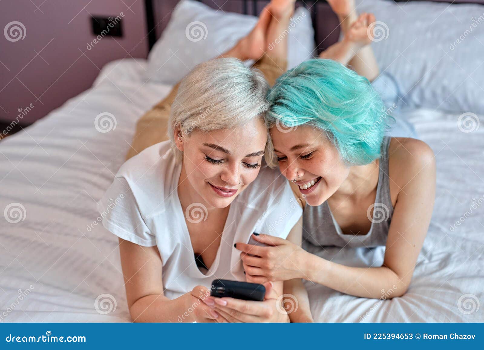 Positive Lesbian Couple Having Sun on Bed Using Smartphone, Watching Video Stock Image