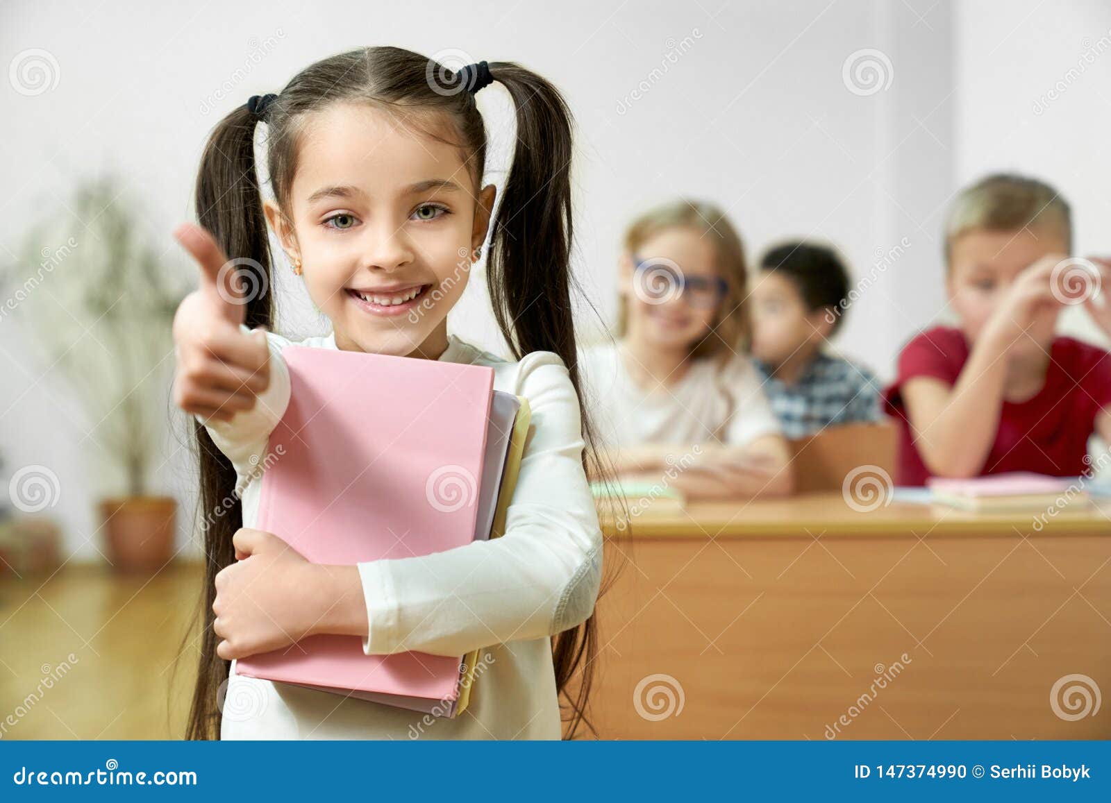 positive schoolgirl holding books and showing thumb up.