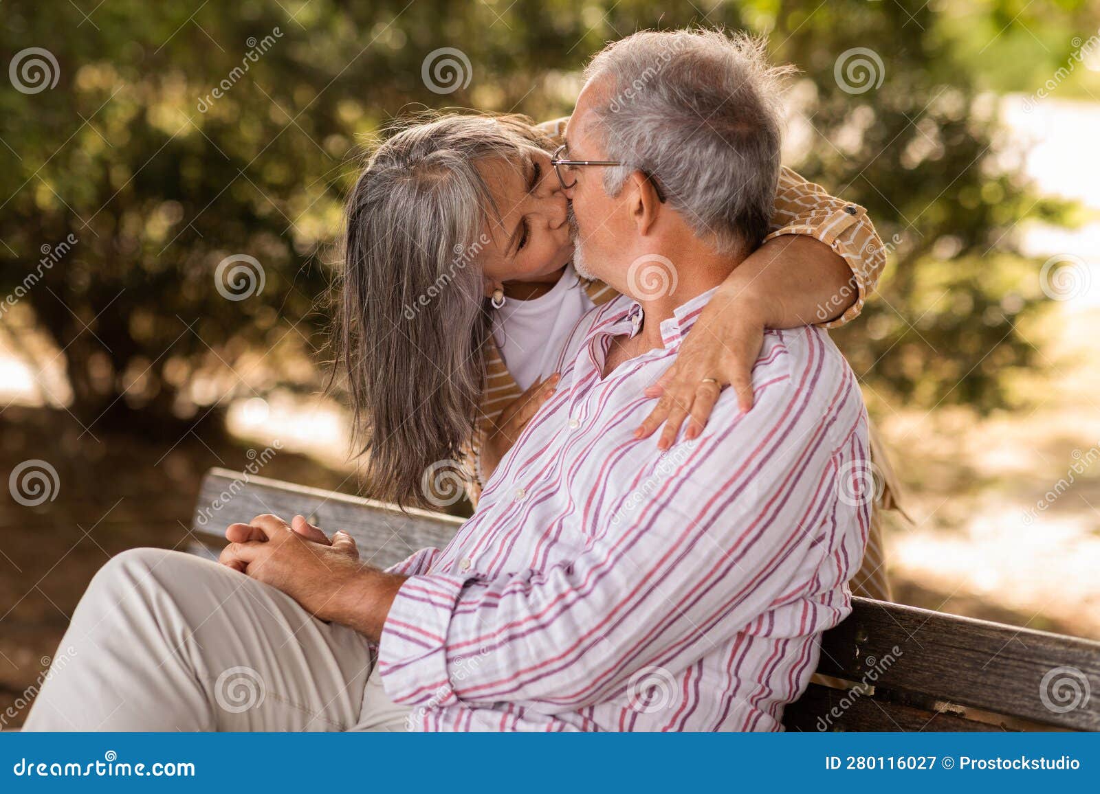 Positive Senior Caucasian Wife Hugs and Kisses Husband, Sits on Bench in Park Stock Image