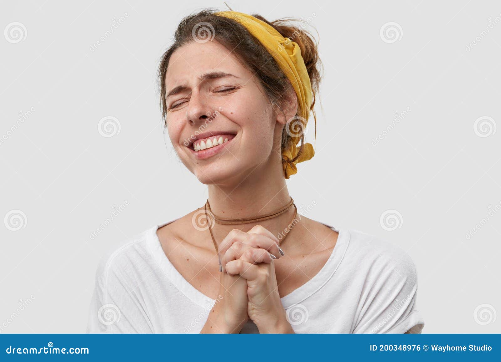 positive wishful young woman keeps palms pressed together, hopes dreams come true, makes wish, wears yellow headband