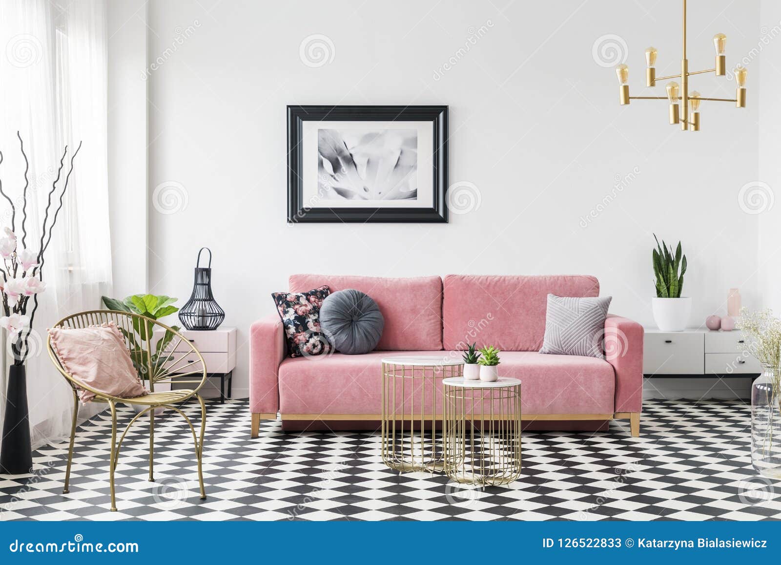 poster above pink sofa in living room interior with gold armchair on checkered floor. real photo