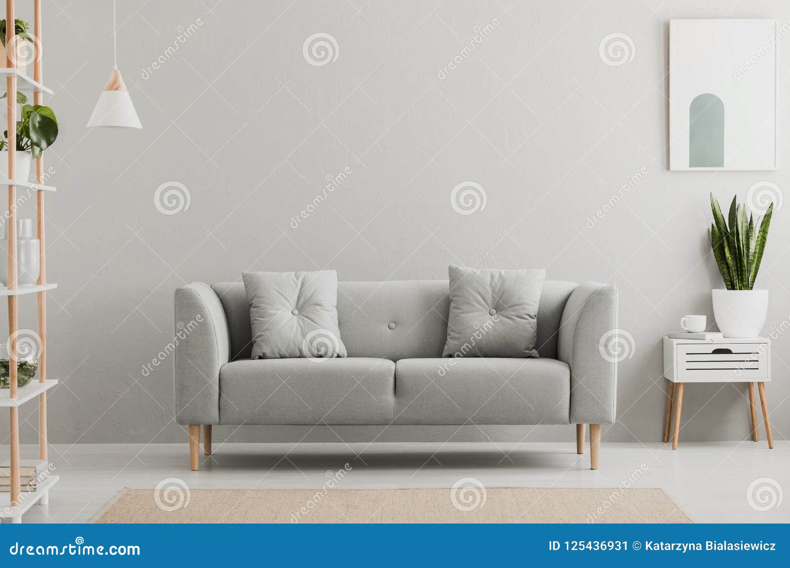 poster above white cabinet with plant next to grey sofa in simple living room interior. real photo