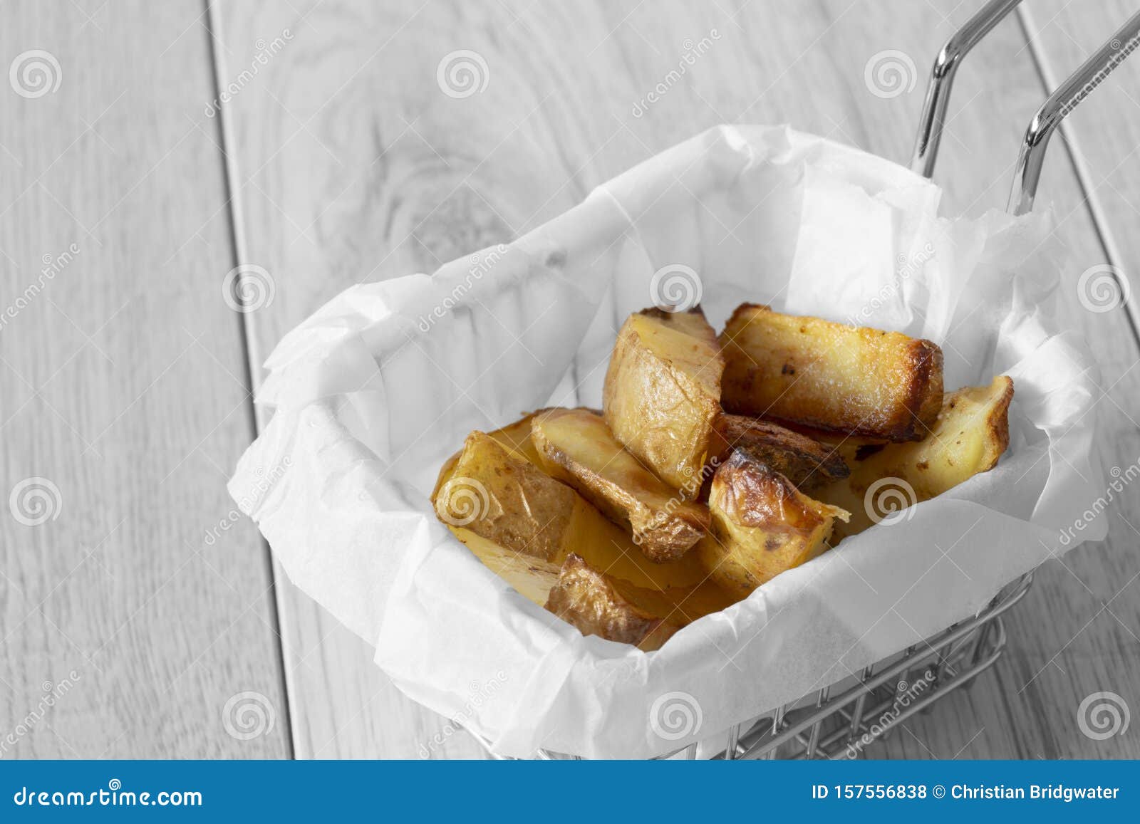 potato wedges chips in a wire mesh serving basket with greaseproof paper.