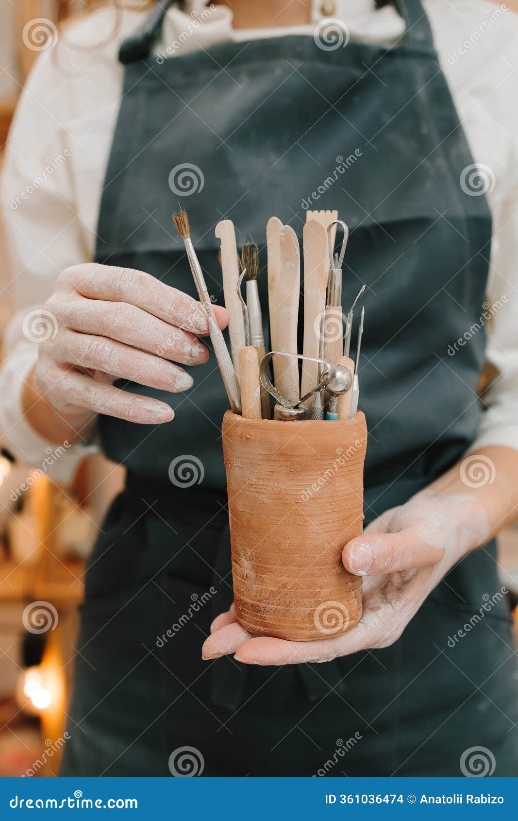 potter in black apron holds a bunch of instruments for sculpting pottery in ceramic mug. clay crafting tools for