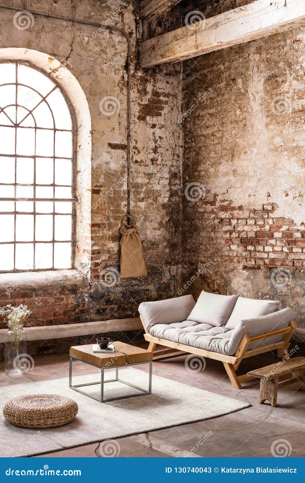 pouf and table on rug in front of wooden sofa in spacious loft interior with window