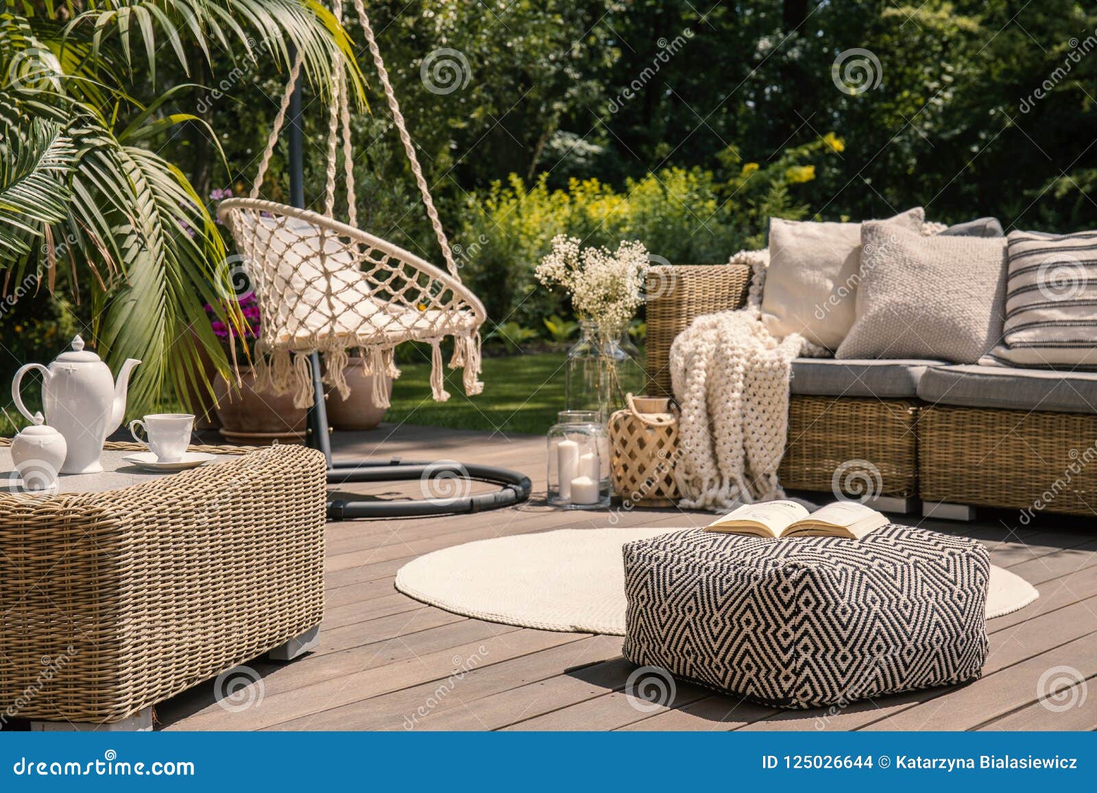 pouf on wooden terrace with rattan sofa and table in the garden with hanging chair. real photo